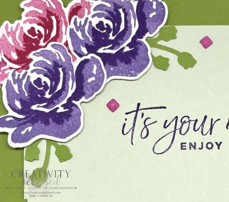 Up-close view of a birthday card using bright green, two shades of purple and two shades of pink on three flowers in the upper left corner. Stamps by Stampin' Up!